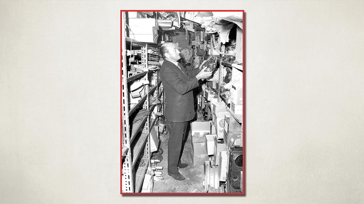 Fred Draper, founder of A H Spares, standing in the stores holding an Austin Healey part
