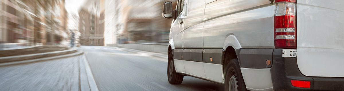 White transit van driving through an urban street in daylight