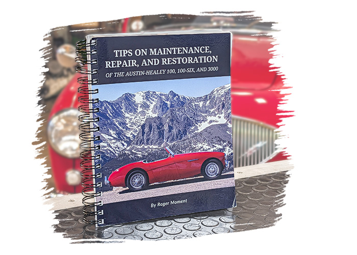 Roger Moment's Austin Healey maintenance and restoration guide open on a workshop bench
