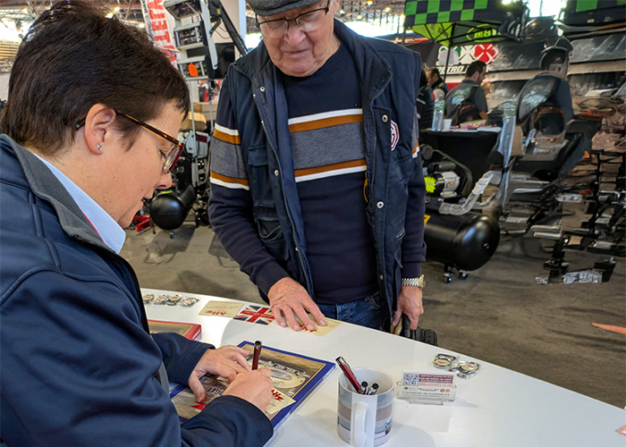 Patricia from A H Spares signing catalogues for visitors at the Époqu’Auto Lyon 2025 classic car show.