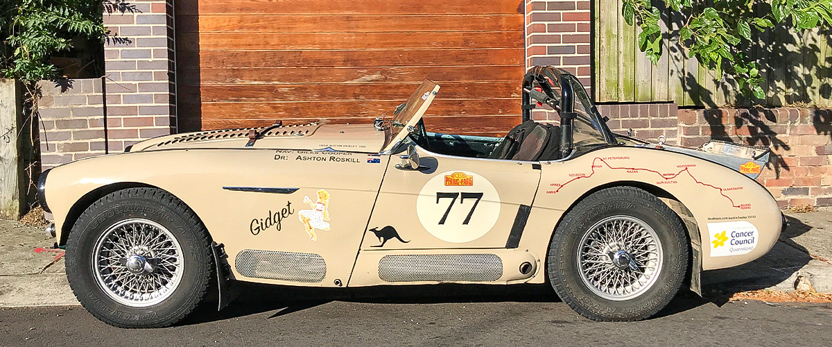 Red Austin Healey 3000 driving down a road