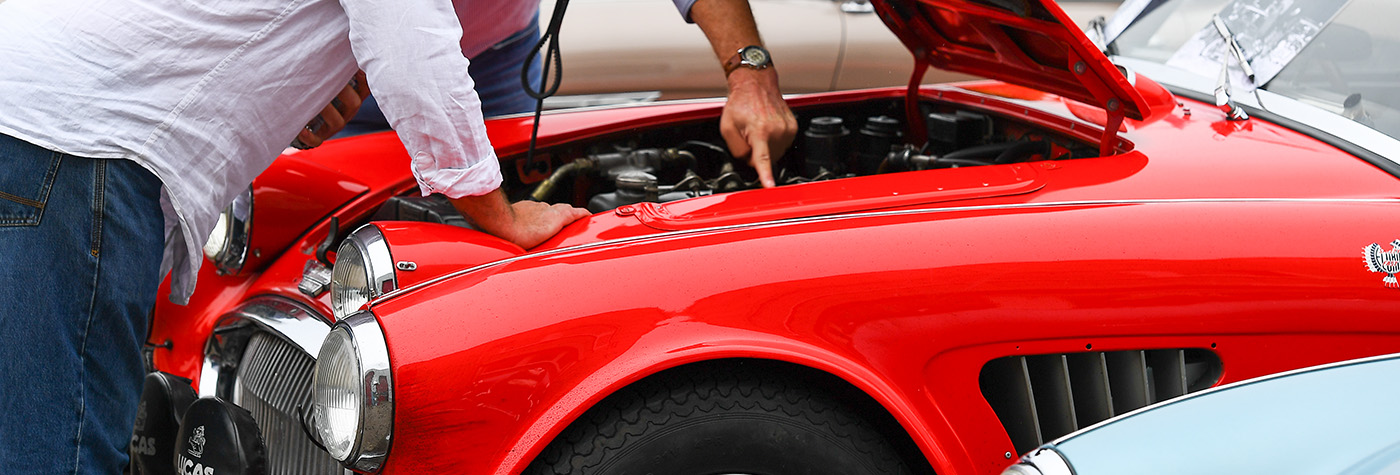 Two men examining the engine bay of a red Austin Healey 3000
