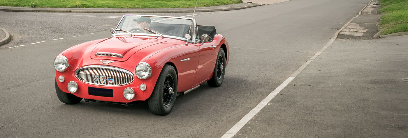 Red Austin Healey 3000 driving down a road