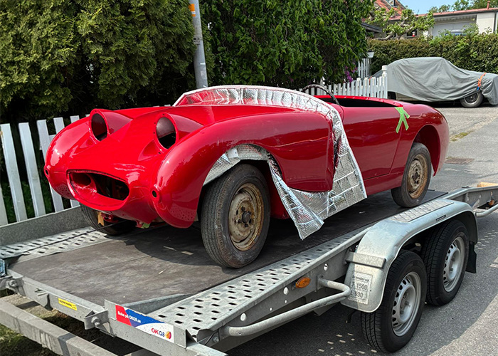 Freshly painted red Frogeye Sprite bodyshell being transported on a trailer during restoration in Sweden.