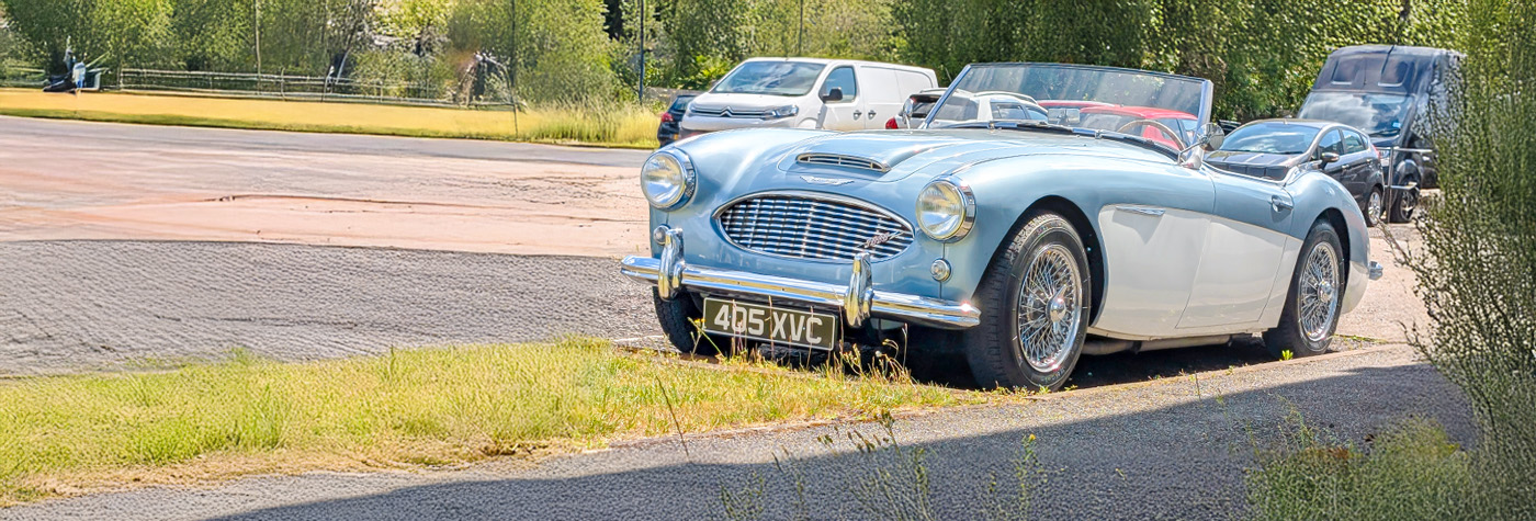 Light blue & white 1957 Austin-Healey BN4 convertible parked on the forecourt in bright summer sunshine.