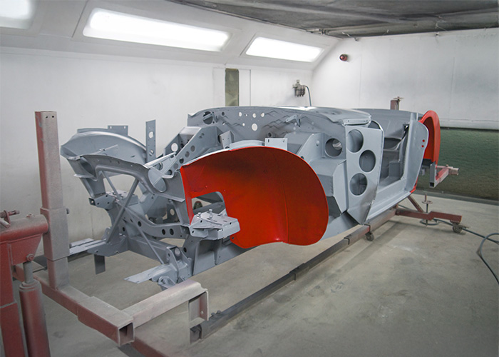 Austin Healey BJ8 chassis in primer and red paint inside spray booth at JME Healeys workshop.