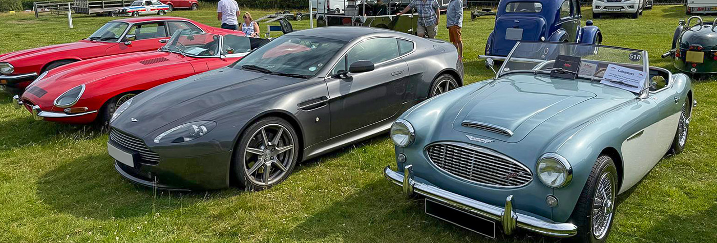 Austin Healey 100-Six next to a modern Aston Martin and Jaguar E-Type