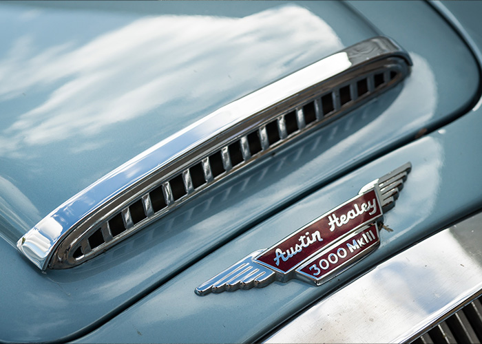 Close-up of an Austin-Healey 3000 MkIII bonnet scoop and badge with chrome detailing under soft daylight.