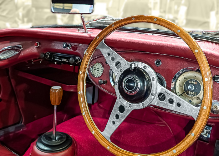 Austin-Healey interior with red trim, wooden steering wheel, Smiths gauges, and period dashboard styling.