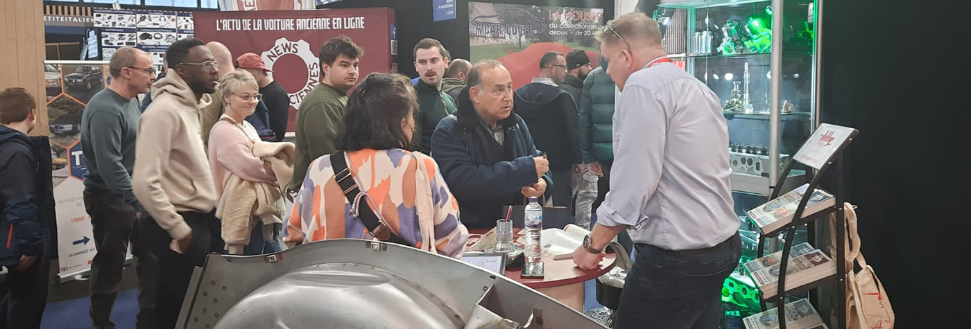 Austin Healey owners discussing restoration projects at the A H Spares stand during Rétromobile 2026 in Paris.