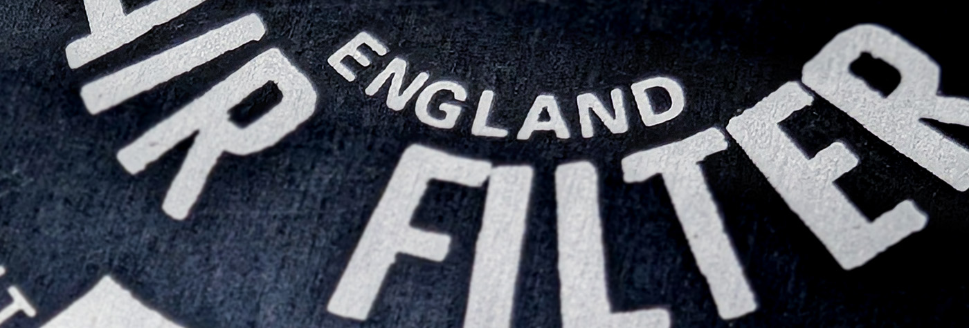 Macro view of Burgess Air Filter plaque showing ENGLAND marking and embossed lettering detail for Austin Healey 100.