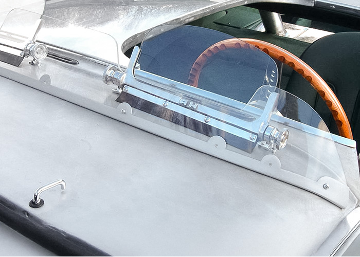 A H aero screen installed on an Austin Healey 100 cockpit, showing raised AH logo and knurled pivots.