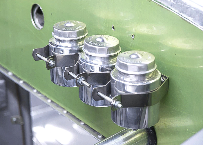 Three polished brake fluid reservoirs inside the engine bay of a classic car
