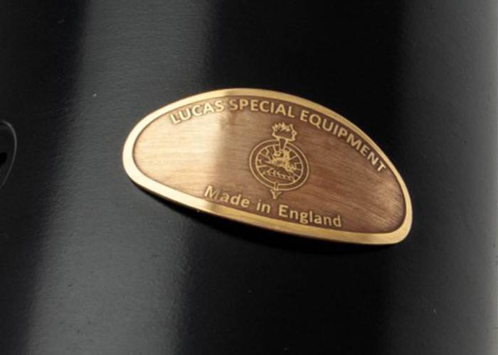 Close-up image of a brass "Lucas Special Equipment – Made in England" identification plaque mounted on a black housing, showing fine engraved detail and satin finish.