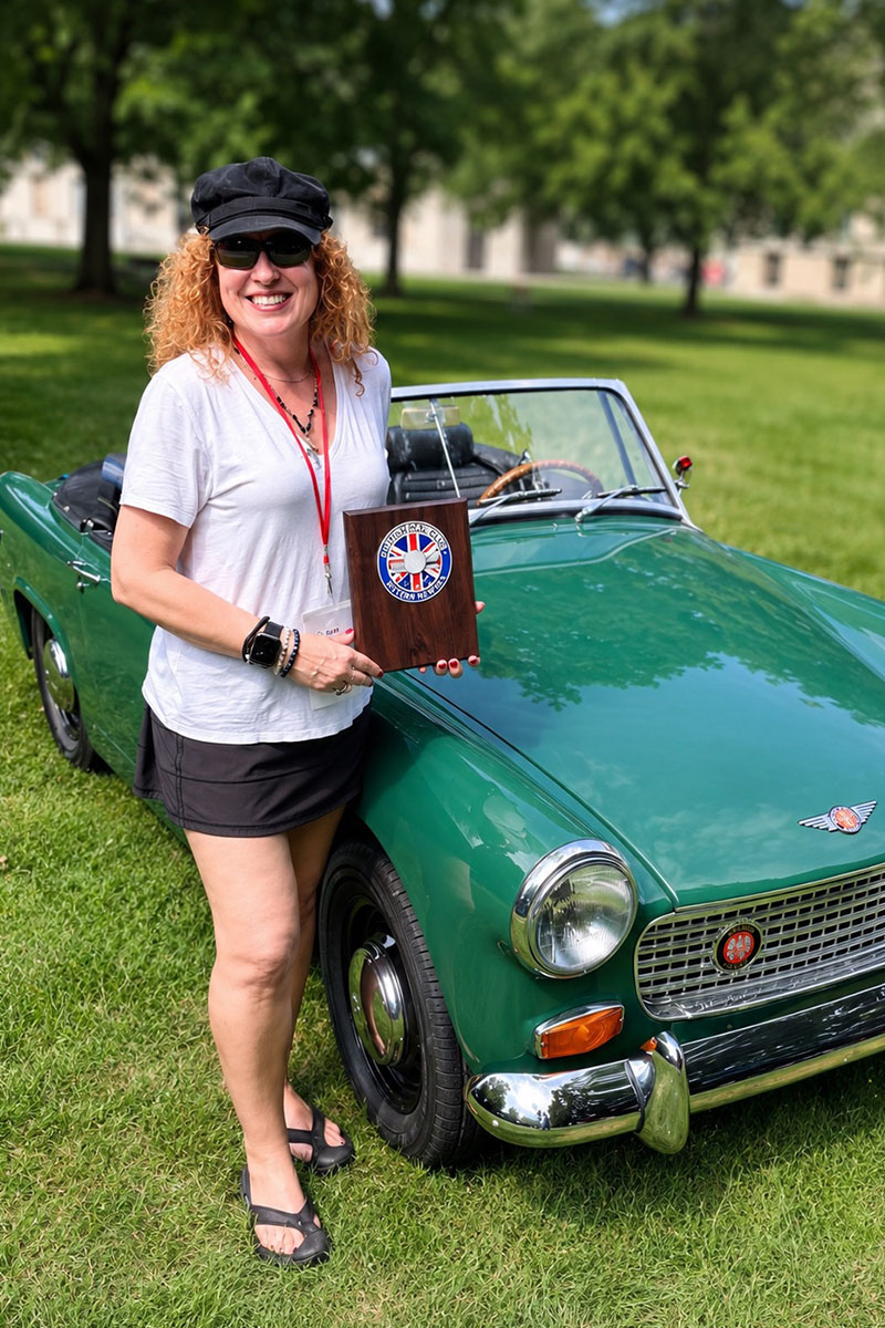 Cari Kalapis beside her restored Austin Healey Sprite with its 1st in Class award at the 2026 Champagne British Car Festival