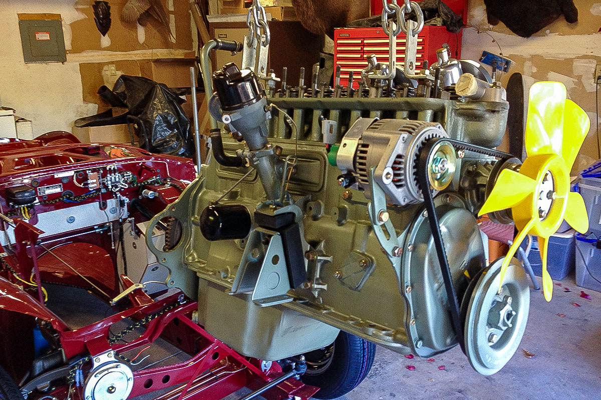 Austin Healey six-cylinder engine suspended beside the painted chassis during reassembly